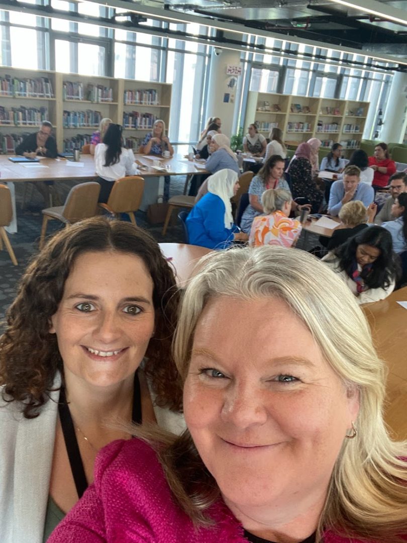 Photograph of a room full of studious adults, with a selfie of beautiful Angela (brown hair, big smile) and Louise (Typical blonde! Heart of Gold!)