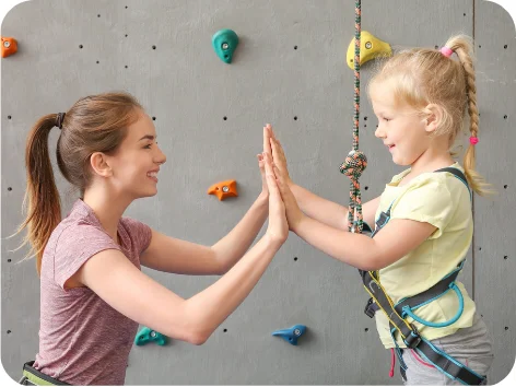 Image of an adult and child clapping hands together near a climbing wall