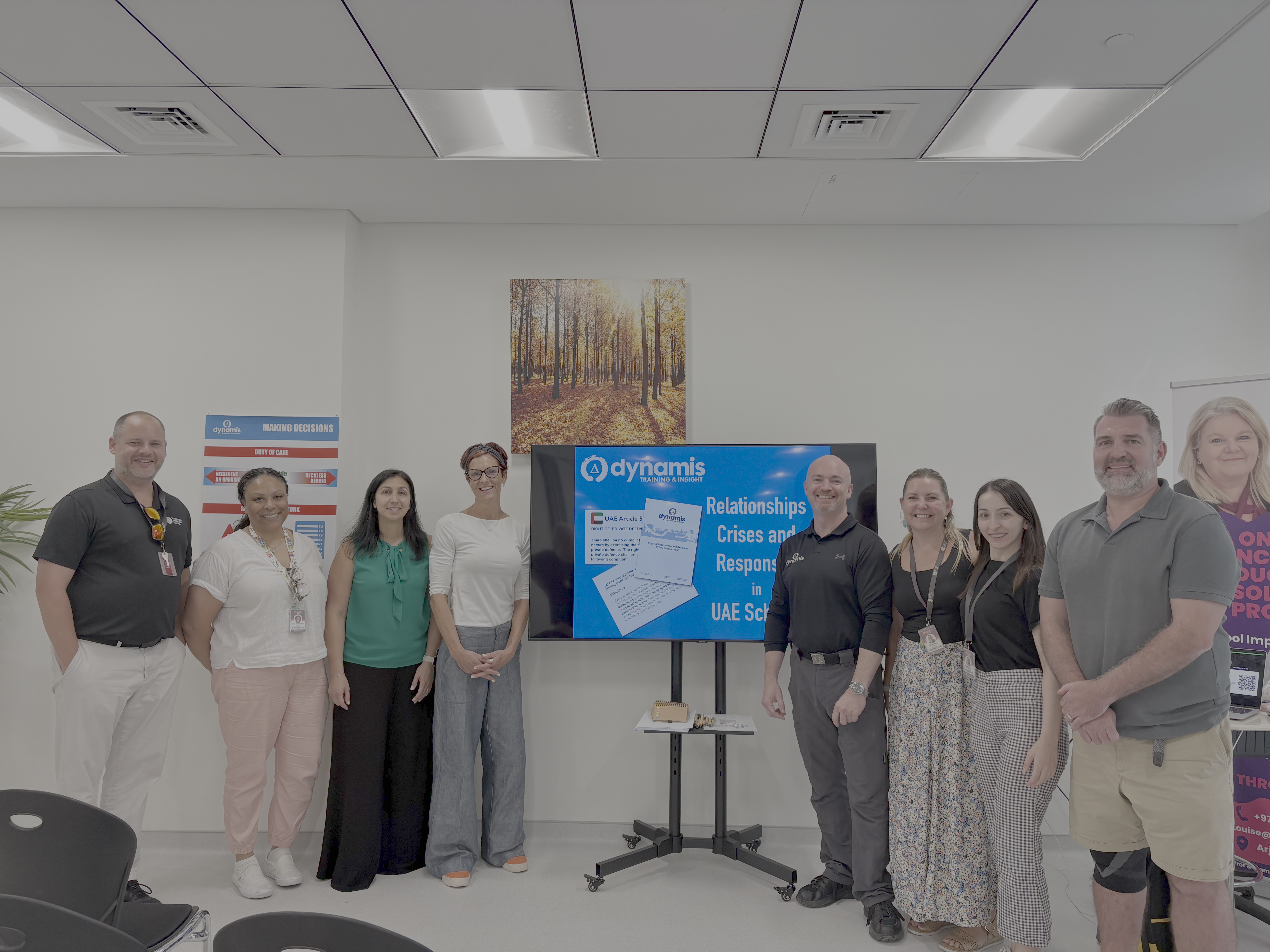 Group photo of Gerard O'Dea (right of the screen, black shirt) and some trainee's from a previous workshop held at Louise Dawson PMDT centre, in front of a screen displaying "Dynamis: Relationships, Crises and Responses in UAE Schools."