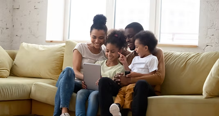 A happy family—mother, father, and two children—sits on a sofa, looking at a tablet together, representing a collaborative approach to identifying a child's needs.