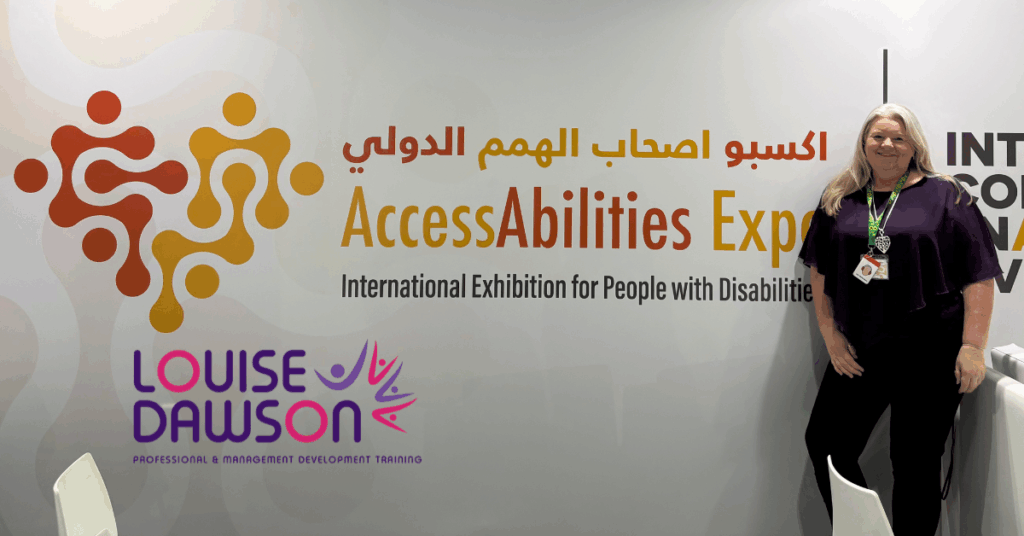 Louise Dawson standing proudly next to the AccessAbilities Expo branding wall, featuring the event logo and the Louise Dawson Inclusion logo, highlighting the partnership.