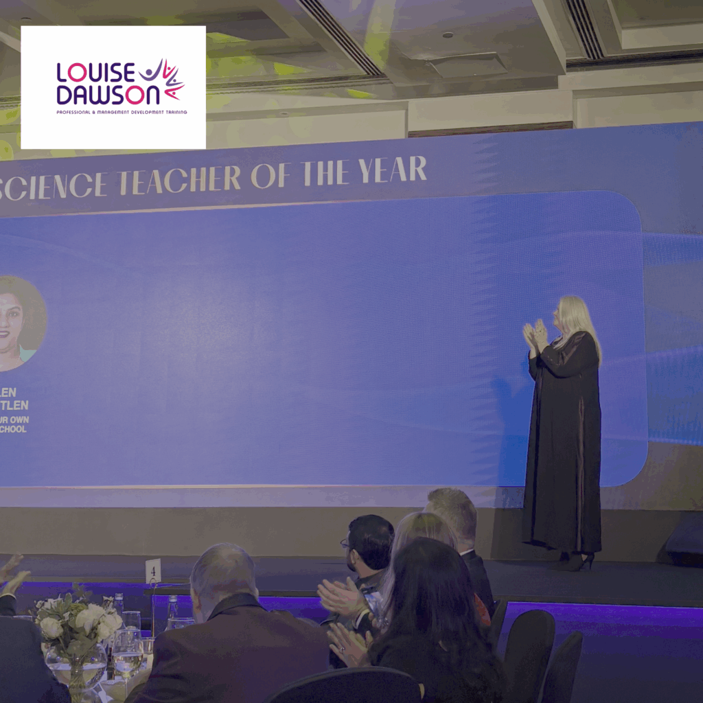 Louise Dawson, an Education Achievement Awards judge, on stage at the gala dinner presenting an award, standing at the lectern with the event branding visible behind her.